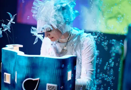 Die Donaunixe sitzt hinter einem Apparat, aus dem jede Menge Seifenblasen strömen.