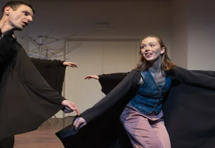 Zwei Performer*innen tanzen mit weit ausgebreiteten schwarzen Umhängen.
