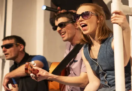 Drei Performer*innen mit Sonnenbrillen musizieren und singen voller Energie.