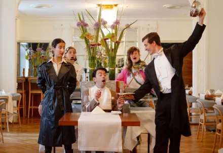 Eine humorvolle Theaterszene in einem eleganten Restaurant – Musik, Chaos und Charme vereinen sich.