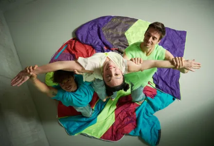 Drei Tänzer formen gemeinsam eine bunte, akrobatische Pose.