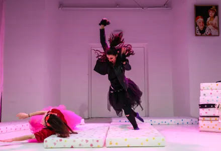 eine in pinkem tüll gekleidete junge frau kugelt sich auf einer matratze am boden, eine in schwarzem tüll gekleidete junge frau lässt sich mit Schwung auf eine zweite Matratze fallen
