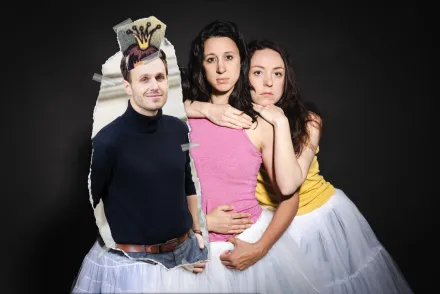 Drei Frauen in weißen Tüllröcken umarmen sich, eine trägt ein pinkes Top, eine ein gelbes Top, und eine eine schwarze Lederjacke