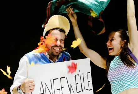 Zwei Personen feiern lachend, während bunte Blätter durch die Luft wirbeln.