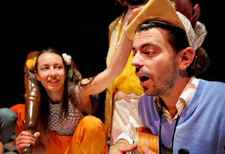 Zwei Performer in bunten Kostümen musizieren und spielen lebhaft auf der Bühne.