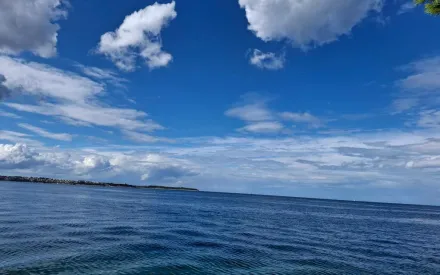 gewässer mit leichten wellen und gekräuselter Wasseroberfläche, blauer Himmer mit Wolken