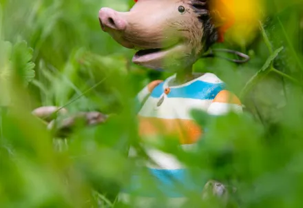 Eine Maulwurf-Figur mit orangefarbener Lampe und gestreiftem Shirt steht zwischen grünen Pflanzen.